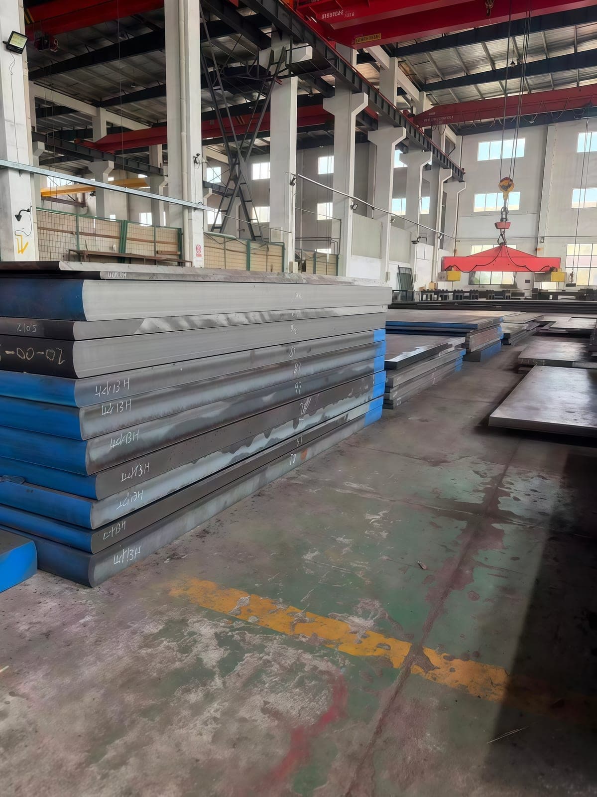 Heavy mold steel plate inventory beneath the workshop lifting equipment.